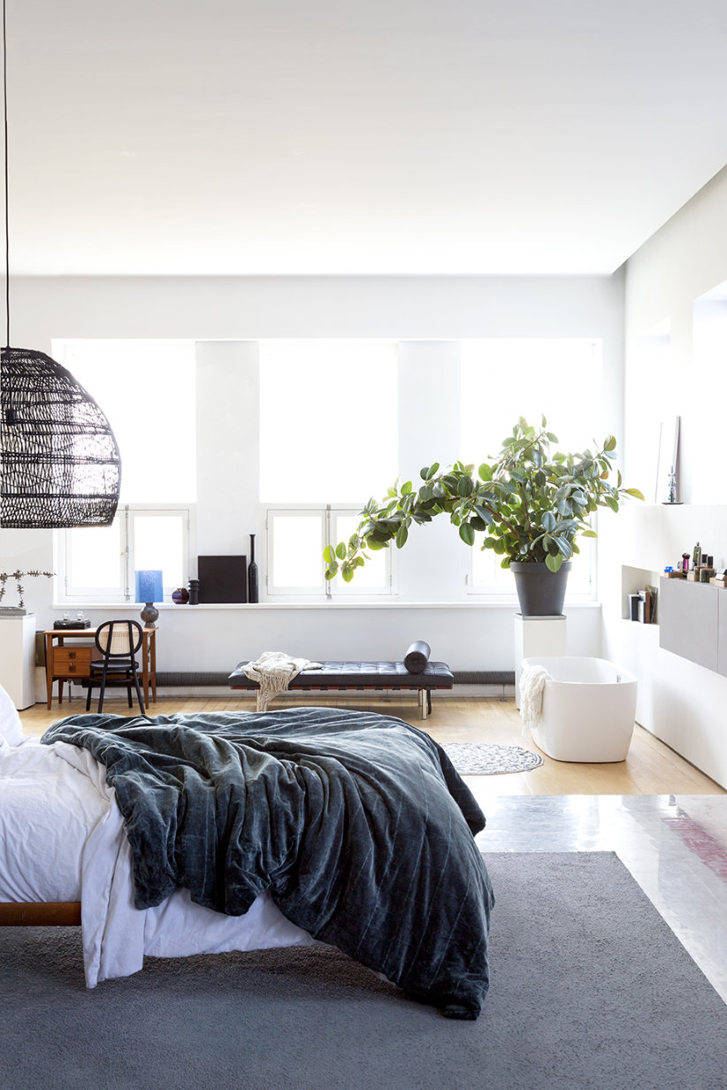 slaapkamer met open badkamer en donkerblauw velours sprei en zwarte rotan hanglamp