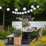 groene tuin met terras en hartman tuinstoelen en lampion lampjes